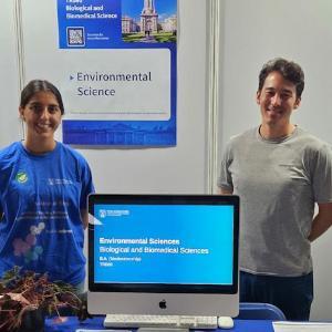 Student and Lecturer standing  smiling at Environmental Science Stand at the Open day 2024. Desk set up with Computer demonstration.